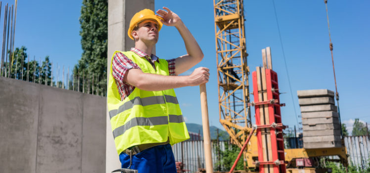 Young blue-collar worker looking up with a worried facial expression while wearing safety equipment during work on the construction site in a sunny day
